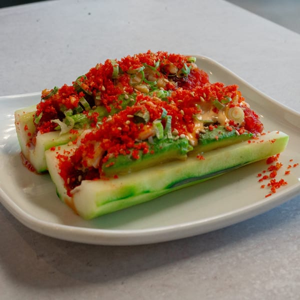 Cucumber slices topped with avocado, red flakes, green onions, and sesame seeds on a white plate.