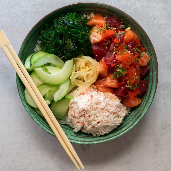 SanSai Japanese Grill poke bowl with salmon, tuna, crab, seaweed, cucumber, and ginger, with chopsticks.
