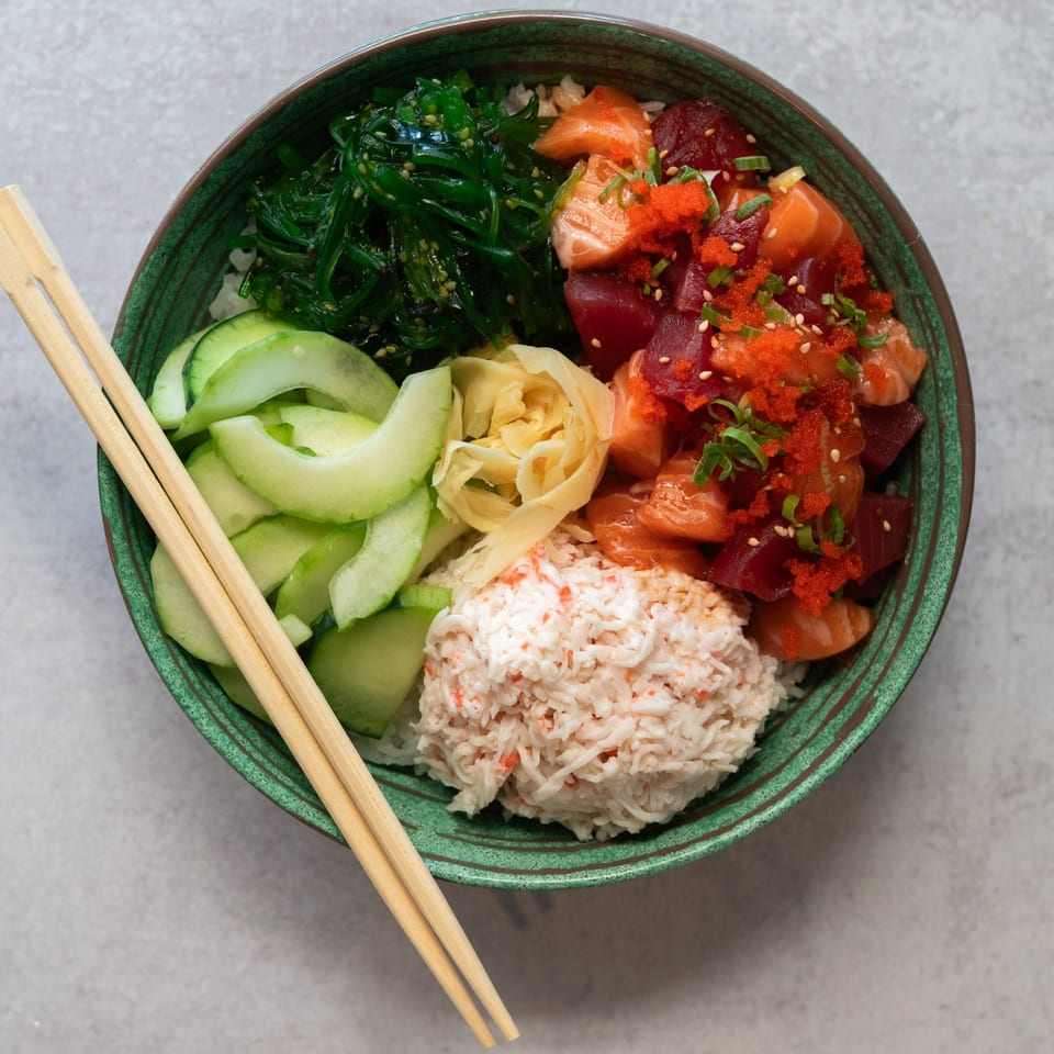 SanSai Japanese Grill poke bowl with salmon, tuna, crab, seaweed, cucumber, and ginger, with chopsticks.