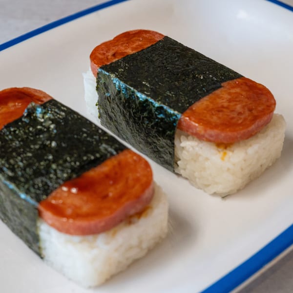 Two Spam musubi, with grilled Spam on top of rice, wrapped in nori, on a white plate.